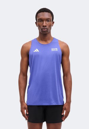 Athletischer Mann mit einem lila ärmellosen BMW Berlin Marathon-Shirt und schwarzen Shorts, stehend vor einem schlichten hellen Hintergrund.