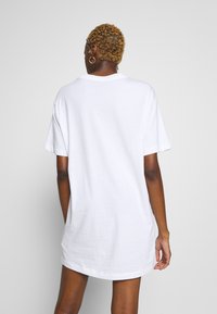 White oversized t-shirt dress, short sleeves, round neckline, soft cotton texture, seamless shoulders, with a straight cut and back.