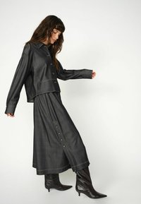 Tmavomodrá džínsová bunda a dlhá sukňa s gombíkmi, s kontrastným prešívaním. Lesklé čierne členkové čižmy dopĺňajú outfit.
