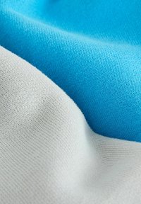 Bavlněná směsová tkanina s hladkou texturou v modré a světle šedé barvě, se jemným pleteným vzorem a měkkým splývavým charakterem.