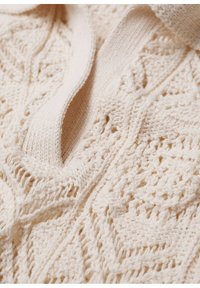 Pull en tricot couleur crème présentant des motifs texturés complexes et un col côtelé doux. Le tissu semble léger mais confortable.