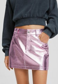 Metallic rosa denim mini kjol med framfickor, knappstängning och synliga sömmar. Matchad med en mörkgrå kort sweatshirt.