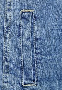 Ljust blå denimtyg med en vertikal rektangulär ficka, synliga sömmar och strukturerad väv.