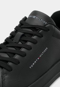 Sneaker din piele neagră Tommy Hilfiger cu sireturi negre, suprafață texturată și text logo pe lateral și pe limbă.