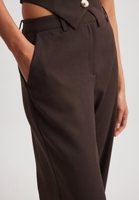 Bruine op maat gemaakte broeken met een soepele textuur, voorzien van zijzakken en een decoratieve knoop op de tailleband.