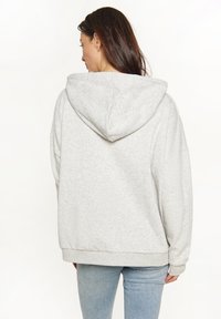 Hellgrauer Kapuzenpullover mit lockerer Passform, weicher Textur, überschnittenen Schultern und gerippten Bündchen, kombiniert mit blauen Jeans.