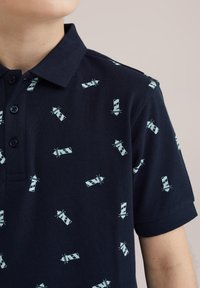 Tengerész kék pamut keverék polo póló, texturált szövettel, világoskék lámpás mintával. Háromgombs stílus és rövid ujjú.