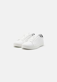 Sneakers bianchi in pelle con superficie liscia, punta tonda e dettagli neri texture sul tallone. Presentano lacci piatti e suola in gomma.