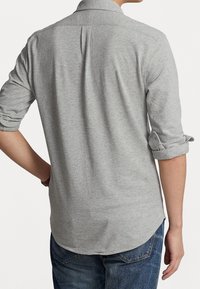 Grå långärmad skjorta med knappfäste, uppvikta ärmar och en enda ryggveck, i kombination med blå denimjeans.