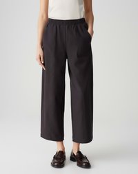 Black, wide-leg pants with a textured surface, elastic waistband, and side pockets, paired with brown loafers and a fitted top.