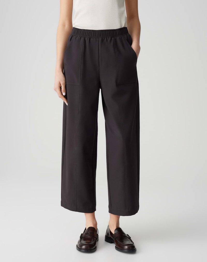 Black, wide-leg pants with a textured surface, elastic waistband, and side pockets, paired with brown loafers and a fitted top.