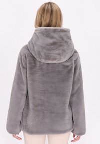 Giacca in finta pelliccia grigia con un grande cappuccio, texture morbida, maniche lunghe e una vestibilità leggermente ampia, caratterizzata da una finitura liscia e un design semplice.
