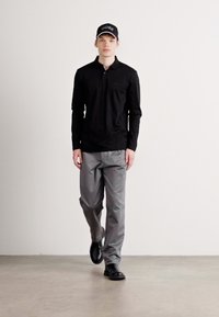 Black long-sleeve polo shirt with a collar, gray trousers, and black shoes. A black cap with white "BOSS" logo on the front.