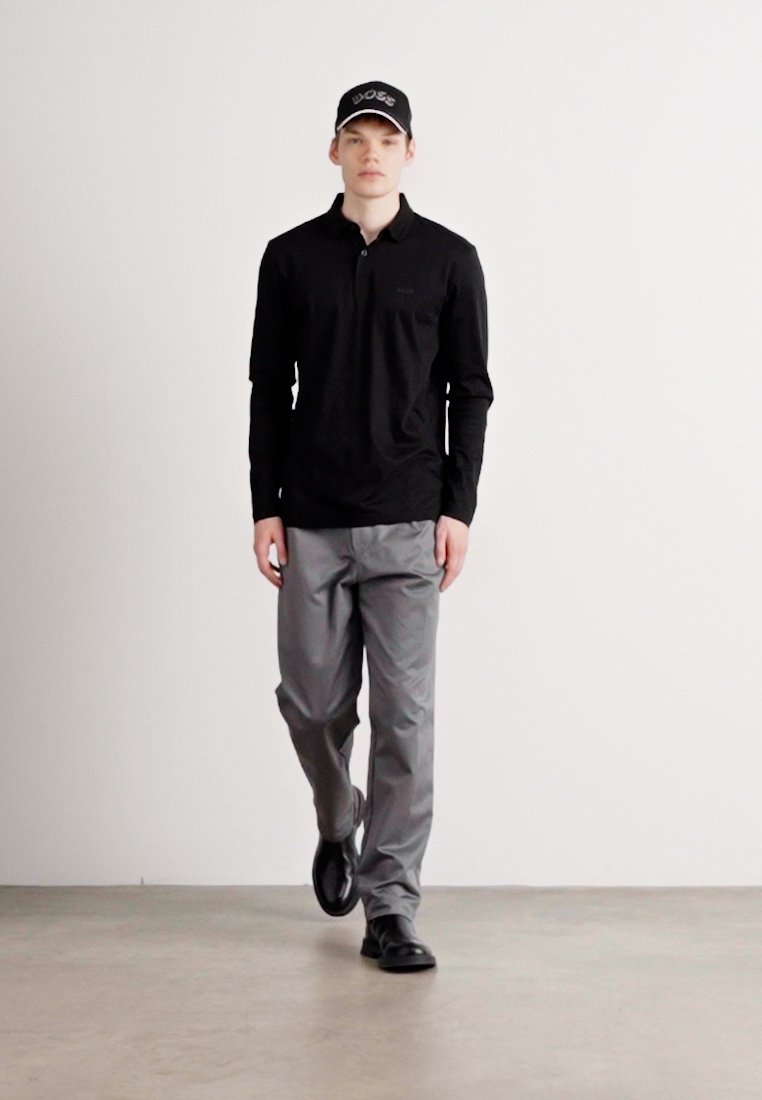 Polo à manches longues noir avec col, pantalon gris et chaussures noires. Une casquette noire avec le logo blanc "BOSS" à l'avant.