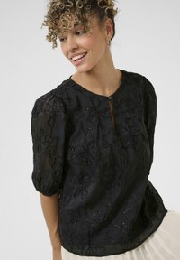 Black blouse made of sheer fabric with puffed sleeves, featuring floral embroidery and bead accents. Keyhole neckline with button closure.