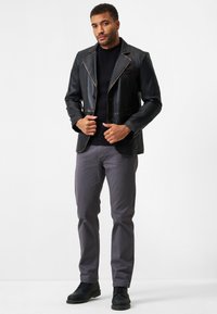 Schwarze Lederblazer mit kontrastierenden Nähten, einer einzelnen Knopfschließe und Reverskragen, kombiniert mit grauen Hosen und schwarzen Stiefeln.