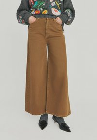 Brune vidde ben jeans med høj talje, lavet af denim, med stitchede kanter og forlommer. Kombineret med grå sokker og sorte heels.