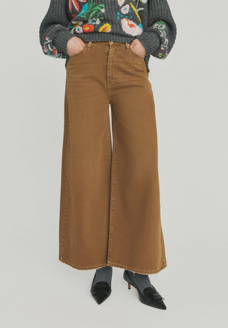 Brune vidde ben jeans med høj talje, lavet af denim, med stitchede kanter og forlommer. Kombineret med grå sokker og sorte heels.