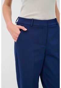 Marineblauwe broek met een rechte pijpdesign, lichte stof en zijzakken. De tailleband heeft lusjes voor een riem, wat een nette afwerking behoudt.