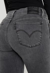Jeans de mezclilla gris con un diseño ajustado, que cuentan con dos bolsillos traseros con costuras en contraste y una etiqueta de cinturón de cuero negro.