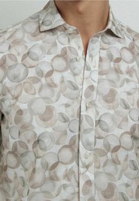 Camisa ligera de botones con un patrón circular perlado en beige y gris, con cuello estándar y textura suave.