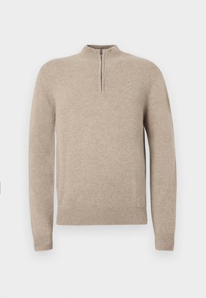 Beiger Strickpullover mit halbem Reißverschlusskragen, gerippten Bündchen und Saum. Glatte Textur mit figurbetontem Schnitt.