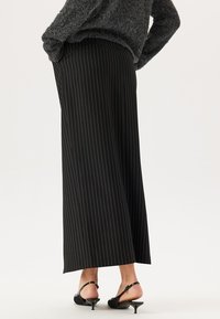 Pantalons larges noirs avec des rayures verticales blanches, dotés d'une taille mi-haute. Associés à des chaussures à talons noires.
