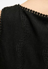 Must räbaline kangas kooreserviga ja peene pitsist kaunistusega kaeluse ümber. Pehmed, silmuslikud aktsendid kaeluse ümber.