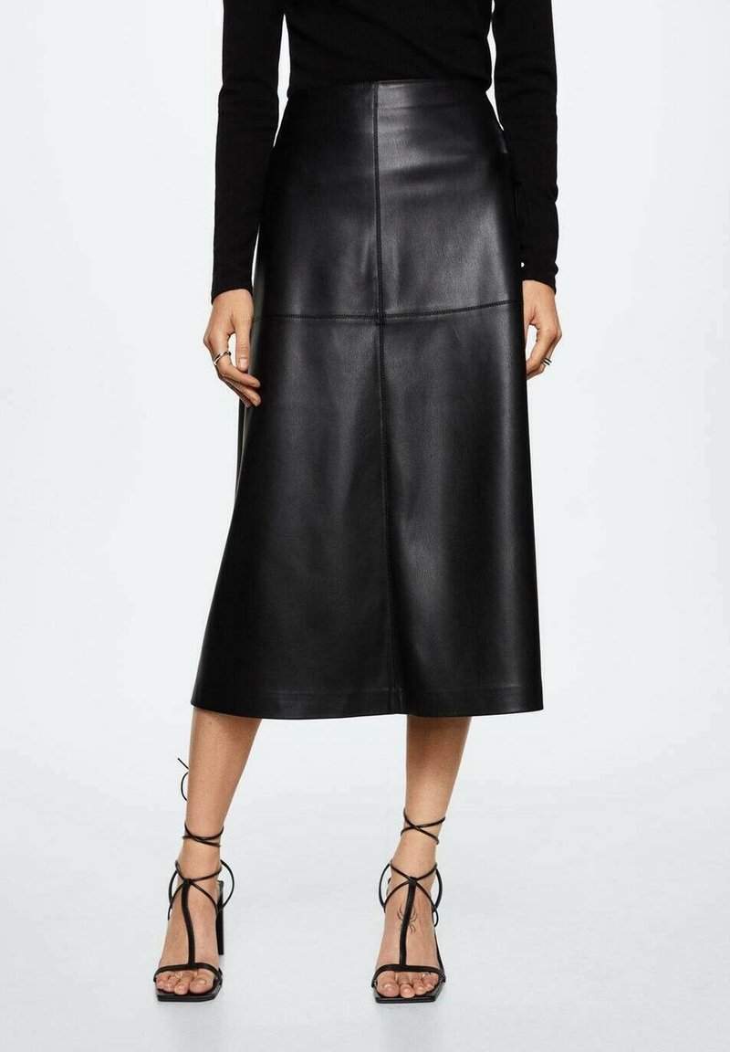 Femme portant une jupe mi-longue en cuir noire taille haute associée à un haut noir à manches longues et des sandales noires à talons hauts et à lanières.