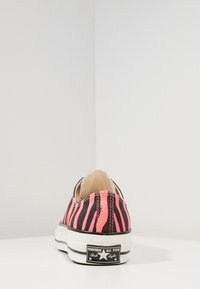 Svart och rosa randig canvas-sneaker med rund tå, vit gummisula och Converse-logotyp på hälen. Strukturerad tygdesign.