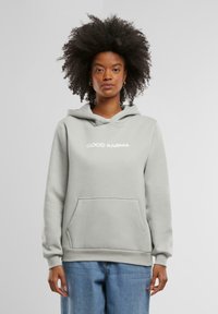 Ljusgrå hoodie med en känguruficka, prydd med vit text "GOOD KARMA" fram, tillverkad av mjukt, strukturerat tyg.