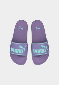 Μωβ πέδιλα Puma slide με ανοιχτό μπλε λογότυπο και κείμενο Puma σε ευρείες λουριά, εμφανίζονται παράλληλα σε λευκό φόντο.