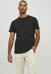 T-shirt nera in cotone con maniche corte e scollatura a girocollo, caratterizzata da un orlo leggermente curvato e un'etichetta nella parte inferiore sinistra.