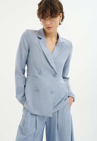 Hellblau, doppelt geknöpfter Blazer mit zwei Knöpfen, taillierte Passform, mit Reverskragen und Seitentaschen. Getragen mit passenden lockeren Hosen.