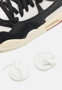 Zapatilla en blanco y negro que presenta materiales de malla y ante, cordones redondos blancos y una suela ligeramente elevada en gris y negro.