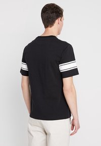 Camiseta negra de manga corta con rayas blancas en las mangas, hecha de algodón, con cuello redondo y un corte relajado.