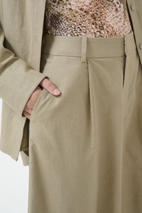 Pantalons kaki avec un devant plissé, des poches latérales et un tissu léger. Portés avec un haut à motifs présentant un design en peau de serpent.