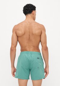 Aquatiske shorts i lys teal stoff, elastisk midje, baklomme med trykknapp, glatt tekstur, midt på låret lengde, minimalistisk design.