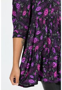 Sort kjole med påfuglefjerprint i lilla og pink, med flæset kant og trekvartærmer. Blød stoftekstur.