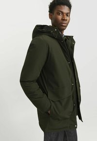 Roheline isoleeritud jakk kapuutsiga, millel on tõmblukk ja nupuvajutused, kaks esikotti ja sile tekstuur.