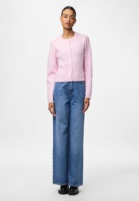 Gaiša rozā ribota kardigāna ar apaļu kakla izgriezumu un pogu aizdari, kas kombinēta ar augstā vidukļa platām džinsām un melniem platformu apaviem.