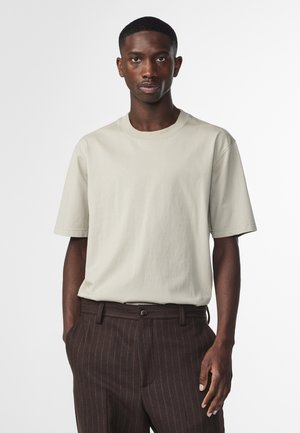 Lys beige bomulds t-shirt med rund hals og korte ærmer, parret med brune stribede bukser, der har en afslappet pasform og en glat tekstur.