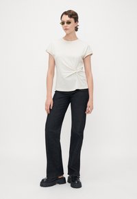 Cream cotton T-shirt with a knotted detail at the waist, paired with black flared denim jeans and chunky black platform shoes.