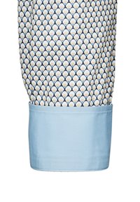 Polsino di camicia abbottonato in tessuto azzurro chiaro, con un motivo di cerchi sovrapposti in navy e crema. Texture liscia, design su misura.