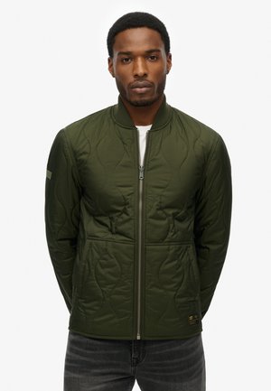 Chaqueta bomber acolchada de color verde oliva con cremallera frontal, cuello acanalado, bolsillos laterales y una etiqueta en el dobladillo inferior. Textura suave.