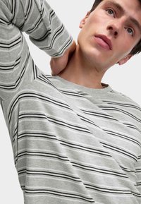 T-shirt a maniche lunghe grigia con strisce orizzontali bianche e nere, scollo rotondo, e materiale in cotone morbido con leggero elasticità.