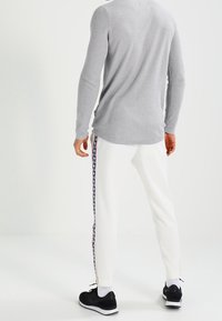 Grå långärmad topp som matchas med vita joggers med ett sidomönstrat rand och svarta sportskor. Slät textur, avslappnad passform.