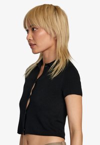 Camisa negra de manga corta con textura, que presenta un frente abotonado y un diseño corto.