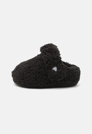 Mule noire duveteuse de style sabot avec une texture pelucheuse et un petit logo alligator sur la sangle latérale.