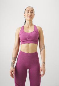 Top corto deportivo rosa con detalle fruncido y leggins de cintura alta a juego. Ambas prendas presentan un tejido suave y texturizado.